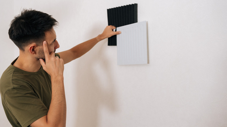 Thoughtful male comparing different soundproofing acoustic panels and placing them on wall for noise reductio