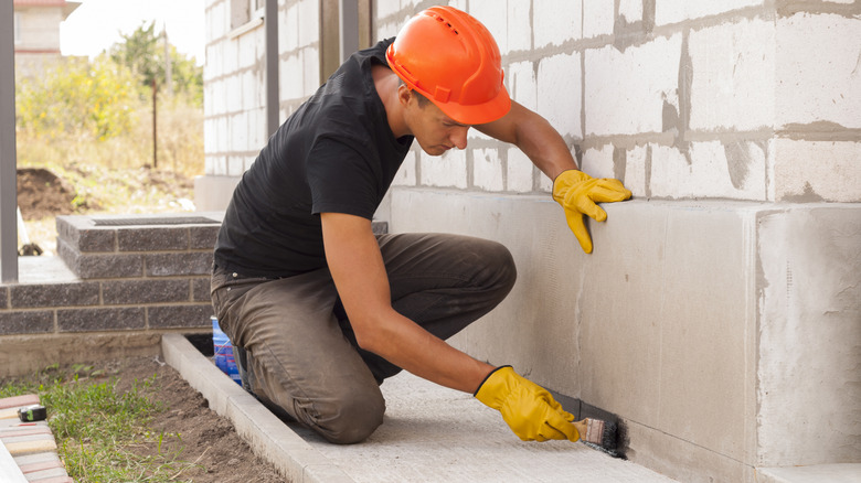 Worker applies sealant to a house foundation.