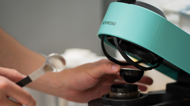 A person putting a pod into a teal Nespresso machine