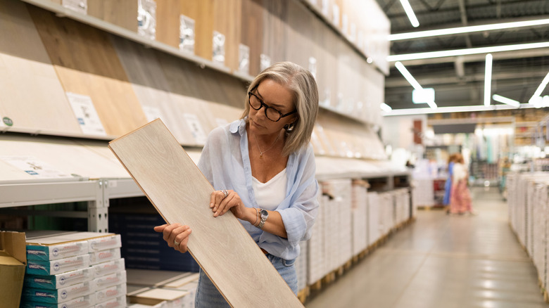 A woman wearing black-framed glasses examines a flooring sample in a hardware store.