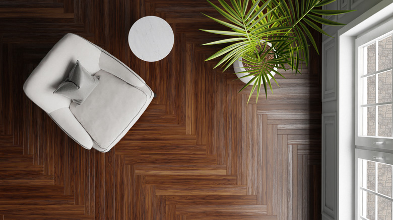 A room with dark timber flooring in a herringbone pattern adorned with a potted palm, a side table, and a single-seater chair.