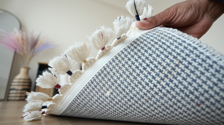 Hand lifting up blue and white rug with tassels