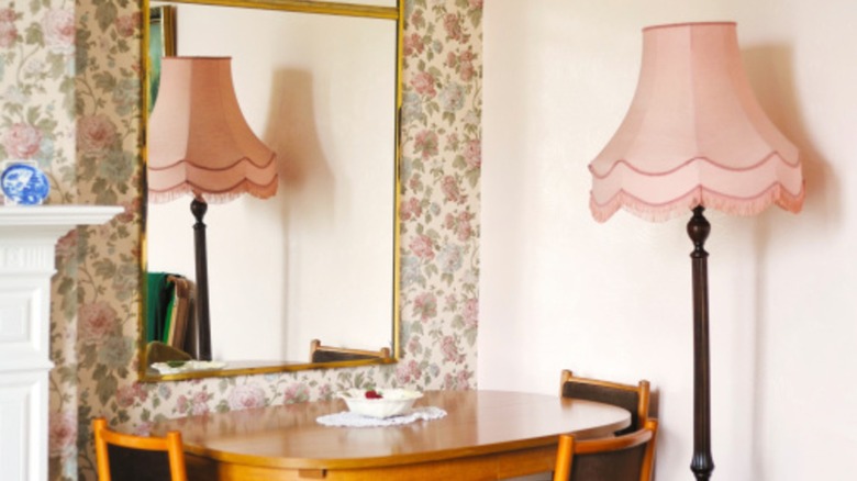 The corner of a 1950s living room has a pink fringed lamp and chintz wallpaper.