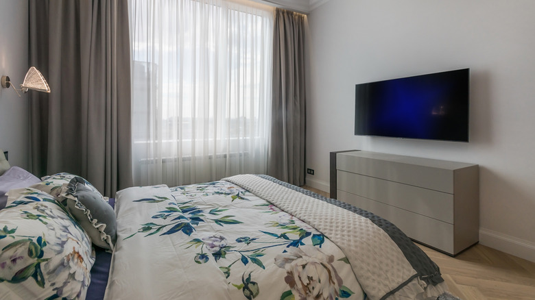 A bed with a white and blue large-scale floral pattern sits in a plain gray bedroom