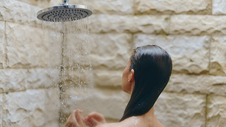Woman stands under a large overhead shower taking a shower.