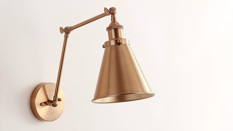 JONATHAN Y faux brass gold wall sconce installed on cream-colored wall