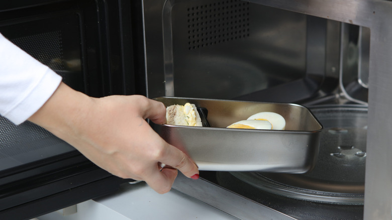 Person's hand sliding metal container into microwave, which could be unsafe.