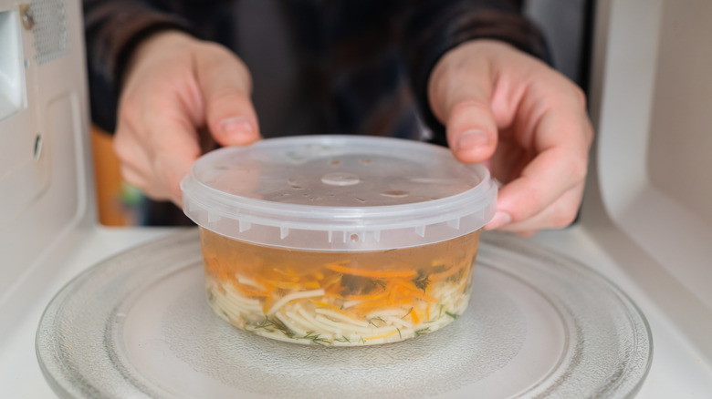 Man's hands placing plastic container with noodle soup in the microwave.