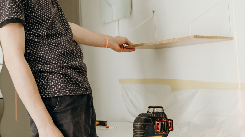 Laser level device being used to straighten hanging wall shelf