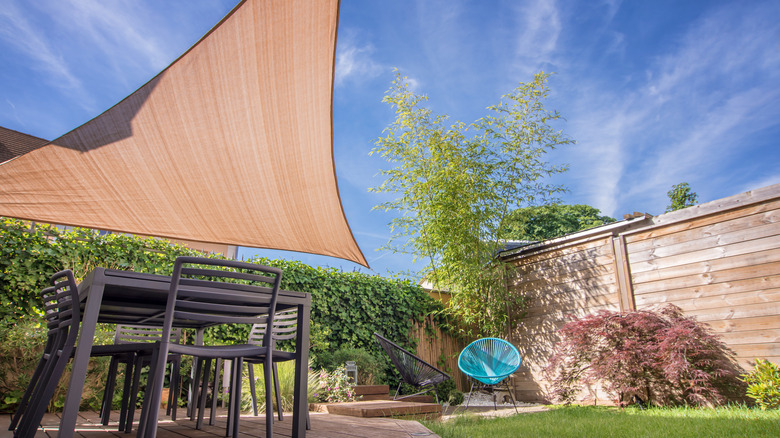 A patio with furniture and a shade sail, plus wood fencing with greenery growing on and around it.