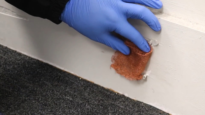 a person uses gloves to install a piece of copper mesh in a mouse hole