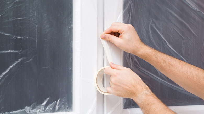 person taping protective plastic over window