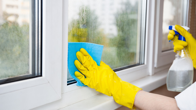 person cleaning window with cloth and spray solution