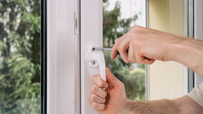 person tightening screw on window