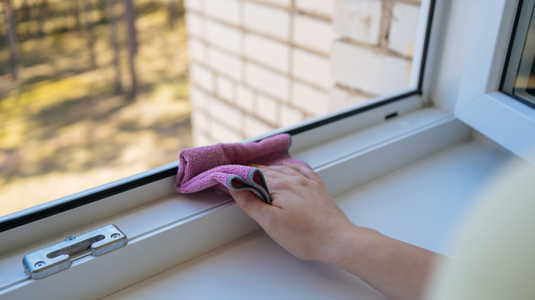 person cleaning window frame with rag