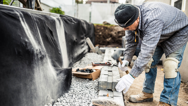 A man building a retaining wall with interlocking concrete blocks