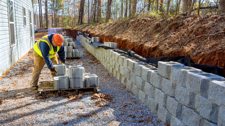 A worker building a retaining wall with concrete blocks