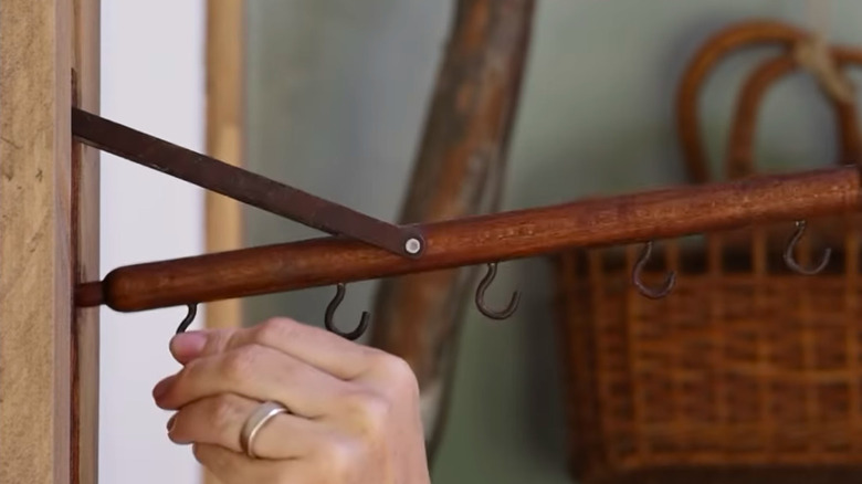 A hand opening a folding valet rack mounted to a wall