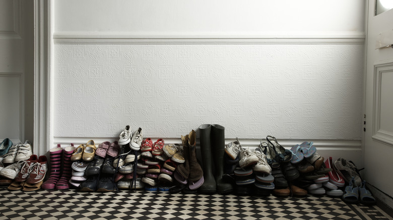 Large pile of shoes stacked against the wall sitting on the floor of a home