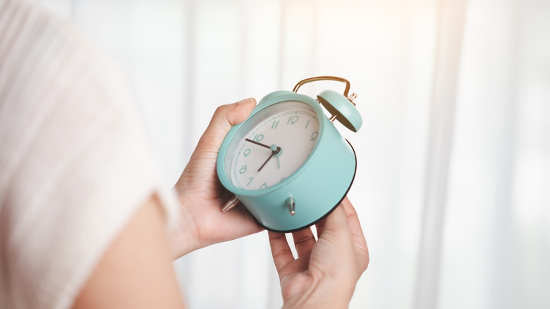 Close up of a person setting a timer on blue alarm clock
