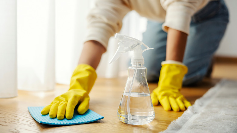 Close up of a person cleaning the floor with a cloth and a spray bottle
