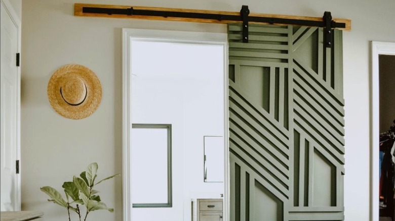 A sage green sliding door with geometric designs made of paneling