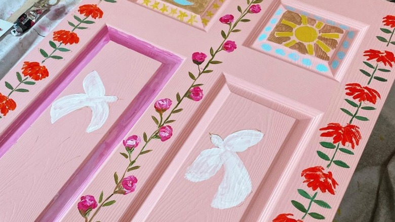 A pink door with painted flower, dove, and sun designs
