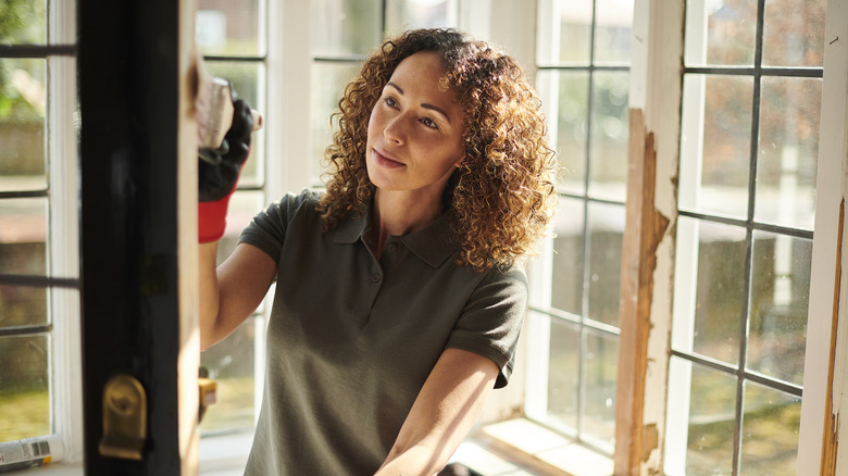 A woman painting a door in a room full of windows