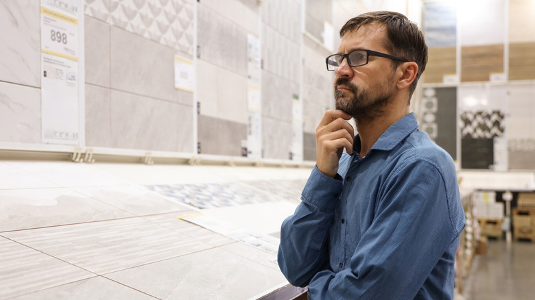 A man looks disappointedly at bathroom tile options in a store