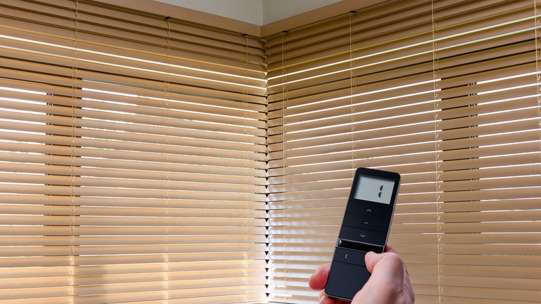 A hand uses a remote to lower blinds.