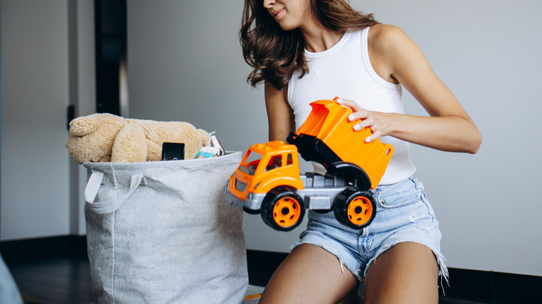 A woman packing away toys in a basic fabric bin.