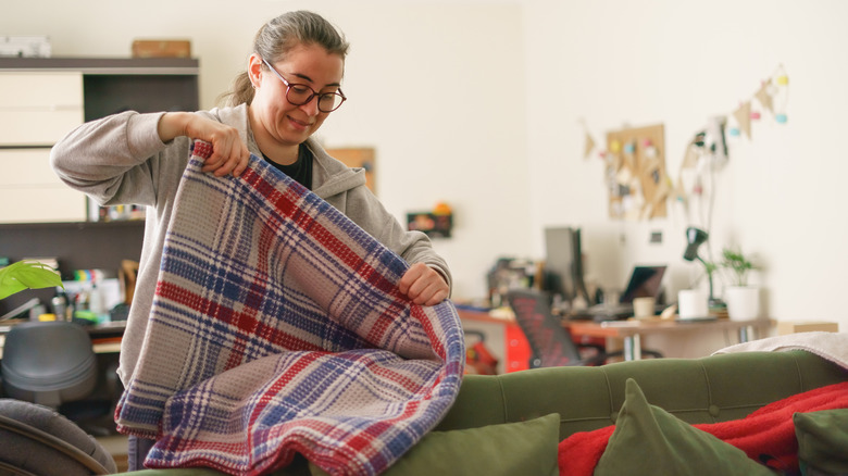 Woman folding a plaid blanket in a living room