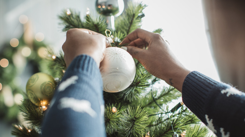 Man hanging up ornaments on a Christmas tree