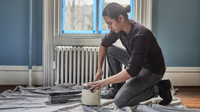 A man opening a can of paint in blue room