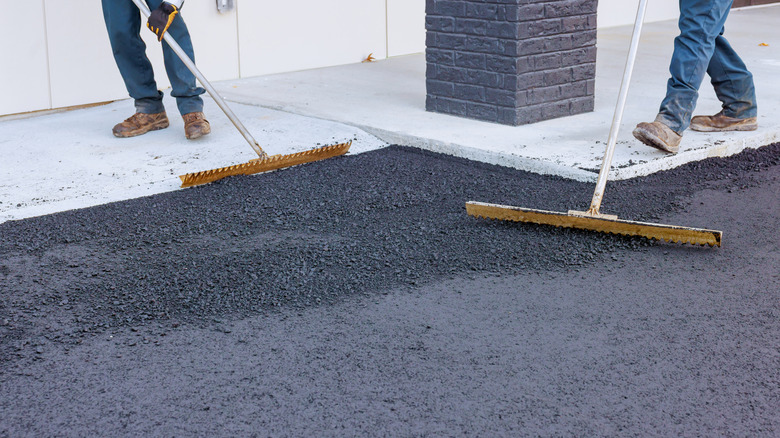 Workers using large brooms to spread fresh asphalt on a driveway