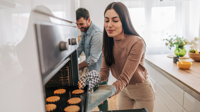 A woman takes a pan full of cookies out of the oven.