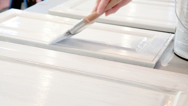 A person painting cabinets with white paint