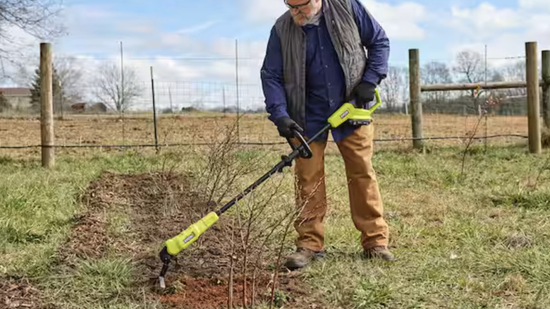 Man using the Ryobi electric garden hoe in a garden bed