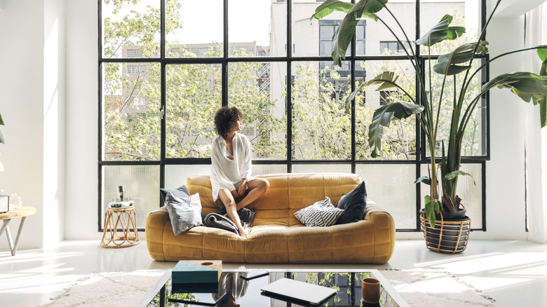 Woman sitting on cozy sofa looking out large window