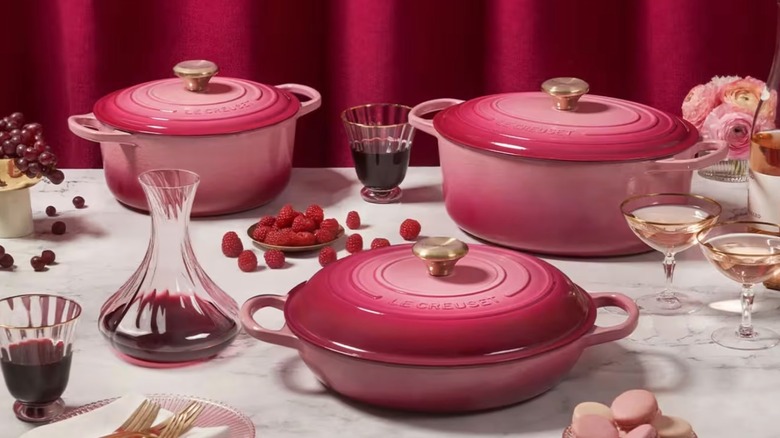 A table set with berry-colored LeCreuset pots, wine, berries, flowers, grapes, and pink macarons.