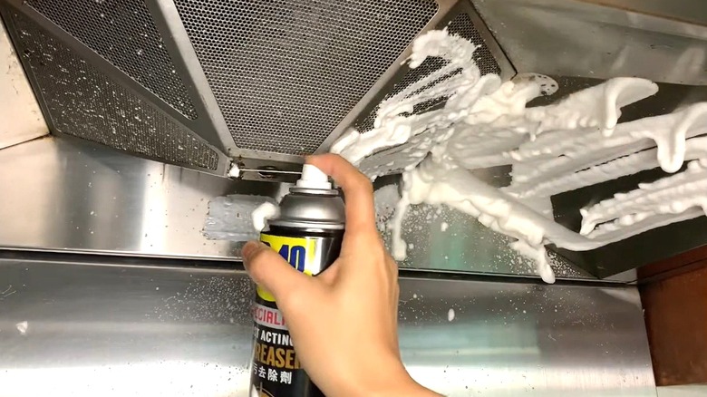 Person uses can of WD-40 degreasing foam to clean range hood.
