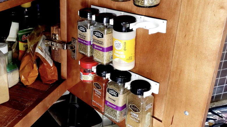 Two strips of plastic spice gripper clips hold jars of spices to the inside of a kitchen cabinet door.
