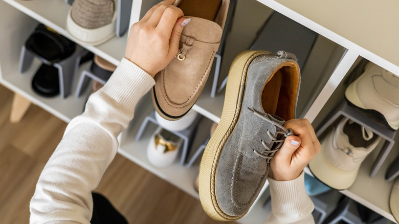 Hands holding two different shoes in closet