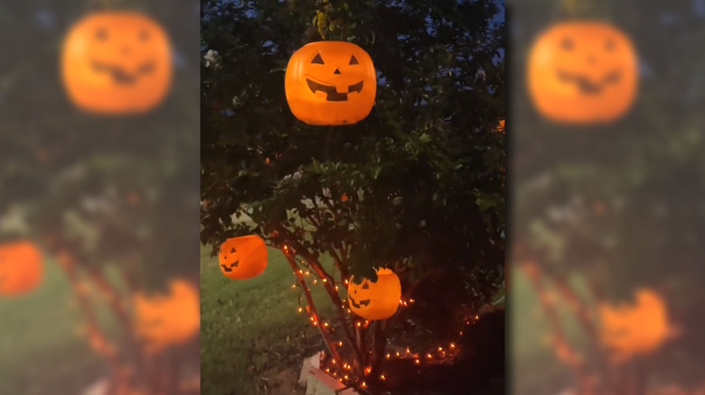 Lit up jack-o-lantern buckets hanging from a tree outside a house