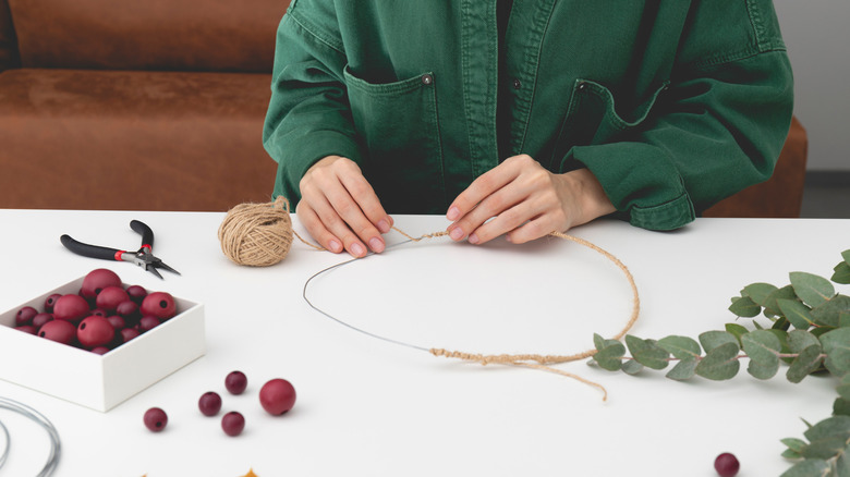 A person makes a fall wreath at a table in their living room.