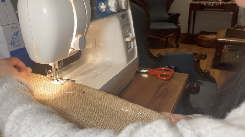Woman sews a seam in burlap curtains on her white sewing machine.