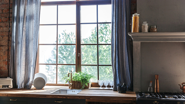 A cozy, rustic kitchen is accented with filmy blue curtains at the window.