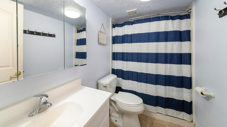 A small bathroom with light blue walls and a blue-and-white horizontal striped shower curtain.