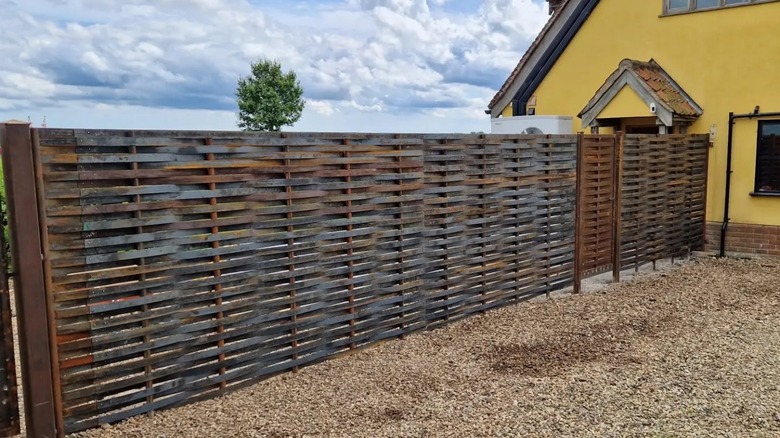 Corten steel fence in various stages of patina next to a yellow home.