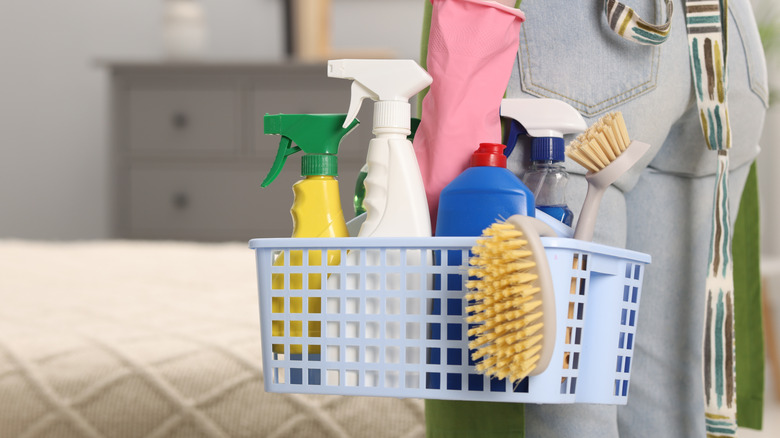 A person holding a basket filled with cleaning supplies in bedroom
